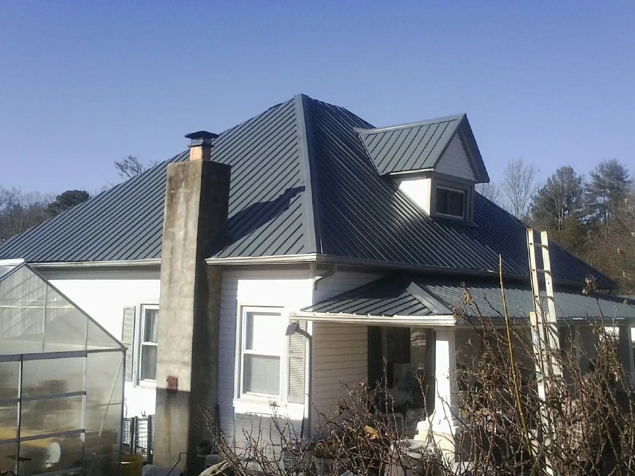 Dark blue standing seam metal roof on a white farmhouse with dormer — Slate & Tile Roof Repair by Roofing Brothers in Orrstown