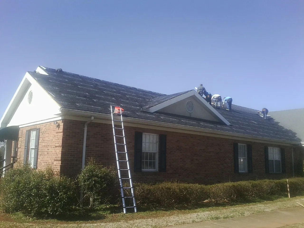 Crew tearing shingles off a brick ranch roof with a ladder set — Emergency Roof Repair work by our crew in Orrstown