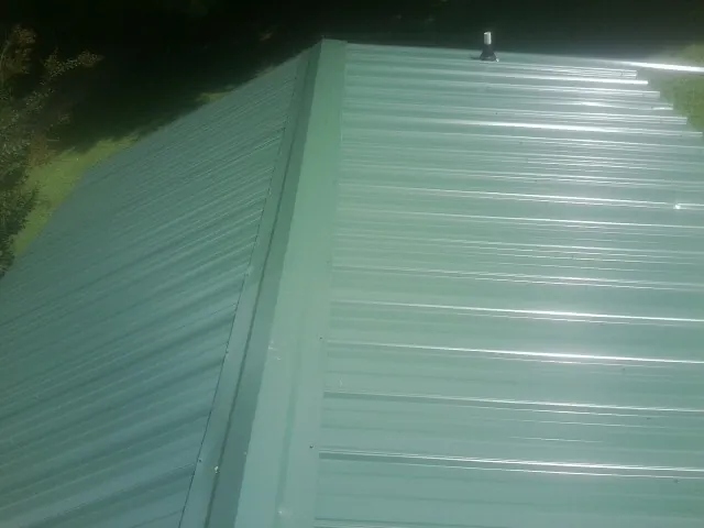 New green metal panels meeting at the ridge of a roof — Flat Roof Repair work by our crew in Orrstown