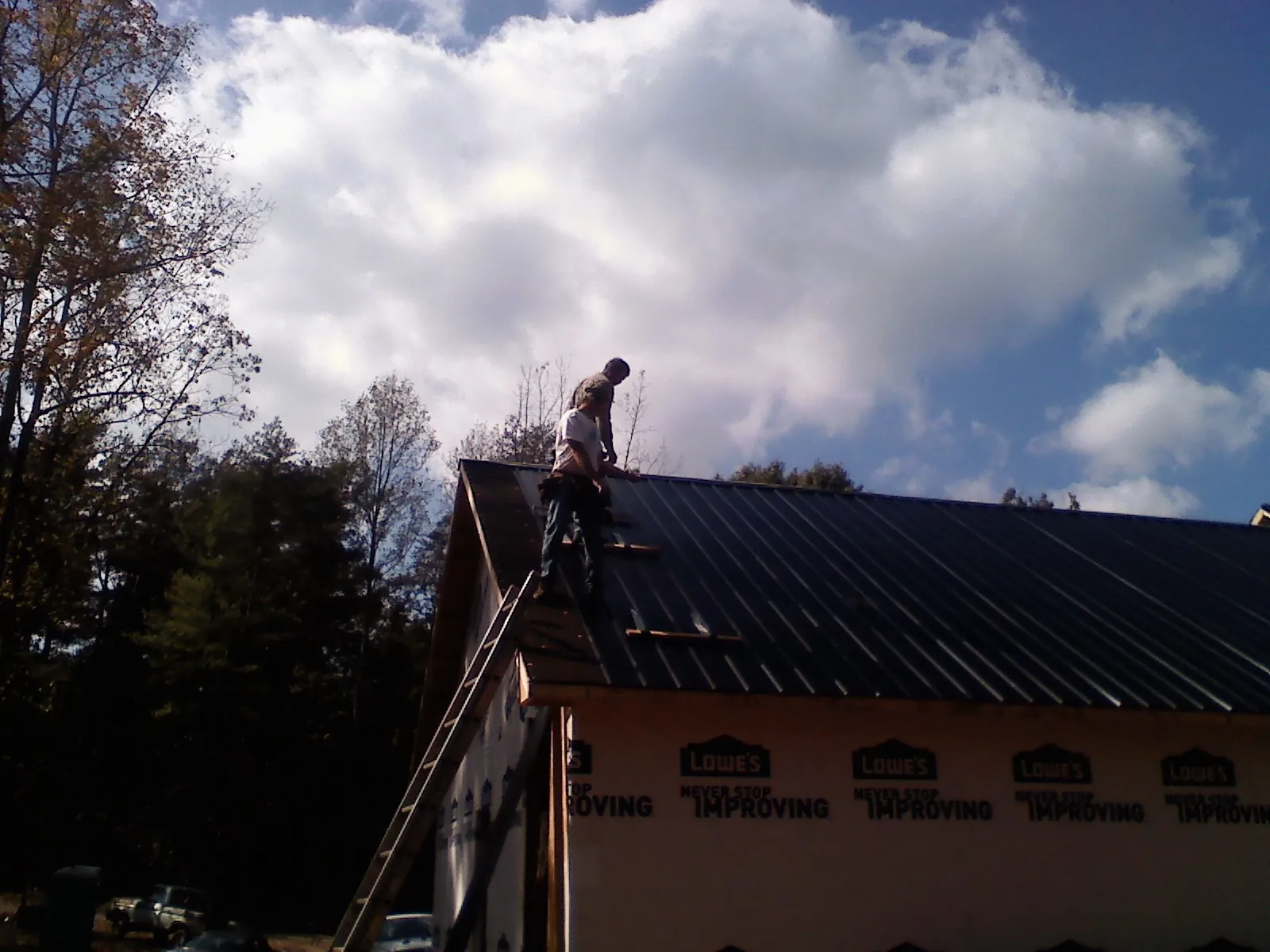 Roofer fastening dark metal panels high against a cloudy sky, from a Roof Inspection job in Orrstown
