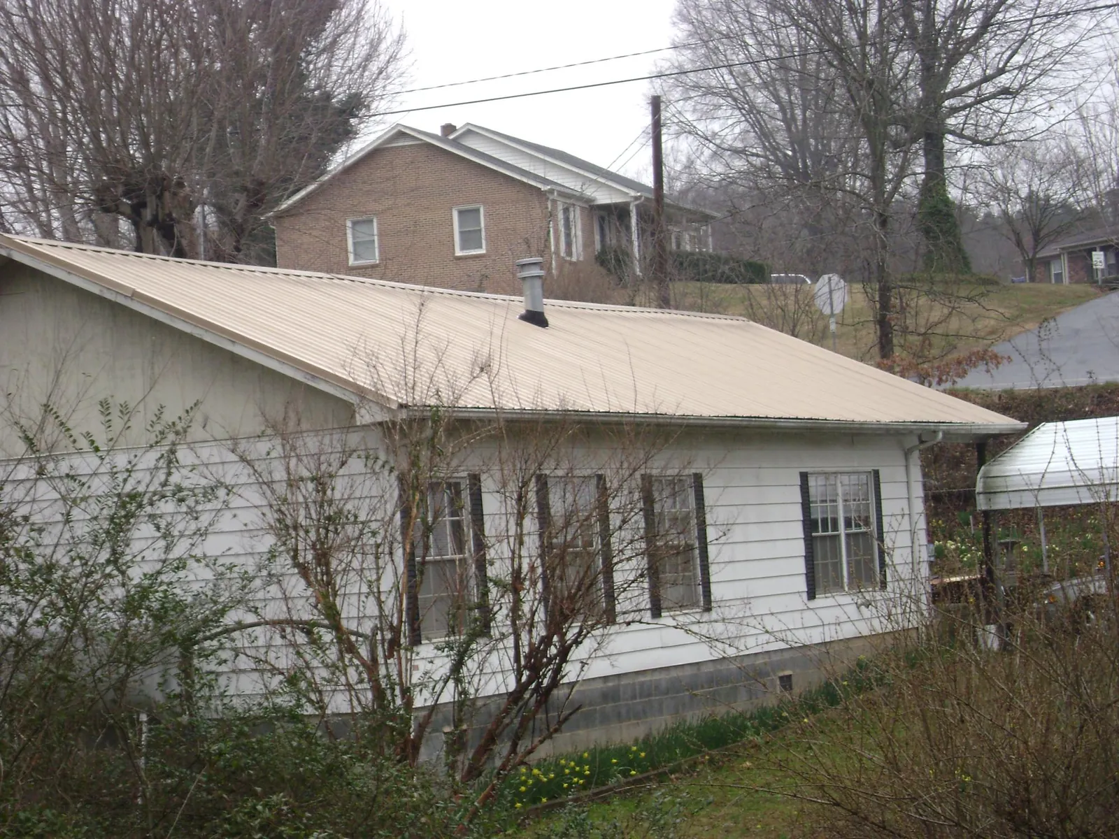 Tan metal roof on a white sided house set into a hillside — Commercial Roofing by Roofing Brothers in Orrstown